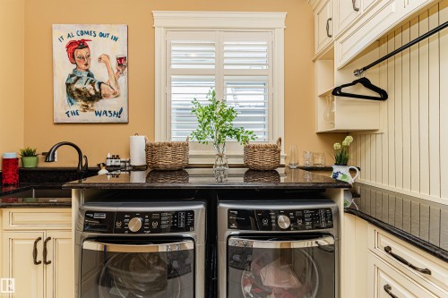 This utility room features cream-colored cabinetry, a granite countertop, a sink with a black faucet, and a window with white shutters - 3048 Watson Landing, Edmonton, AB - Indoor Photo Showing Laundry Room