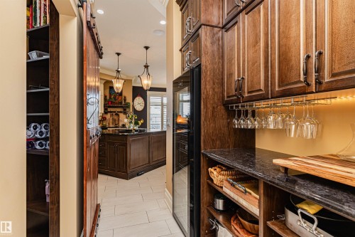 A well-appointed kitchen pantry featuring a wooden barn door, dark wood cabinetry, a built-in wine cooler, and a granite countertop - 3048 Watson Landing, Edmonton, AB - Indoor Photo Showing Other Room