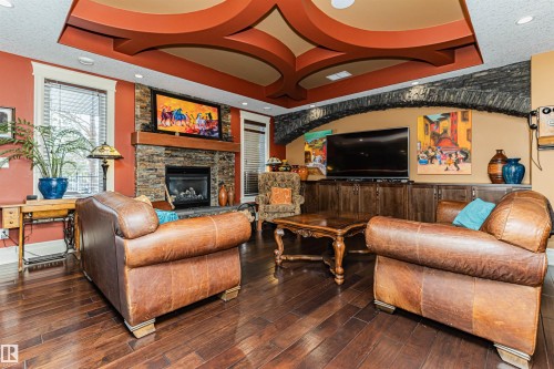 The living area features rich hardwood floors, a stone-faced fireplace with a wooden mantel, and unique ceiling details. - 3048 Watson Landing, Edmonton, AB - Indoor Photo Showing Living Room With Fireplace