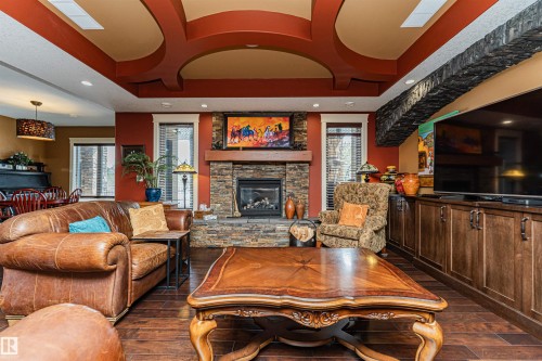The living area features hardwood floors, a stone fireplace, and a custom built-in entertainment unit with cabinetry. - 3048 Watson Landing, Edmonton, AB - Indoor Photo Showing Living Room With Fireplace