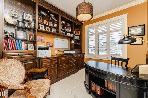 This room features extensive built-in wooden cabinetry with display shelving, a substantial wooden desk, and a large window with white plantation shutters - 3048 Watson Landing, Edmonton, AB - Indoor Photo Showing Other Room
