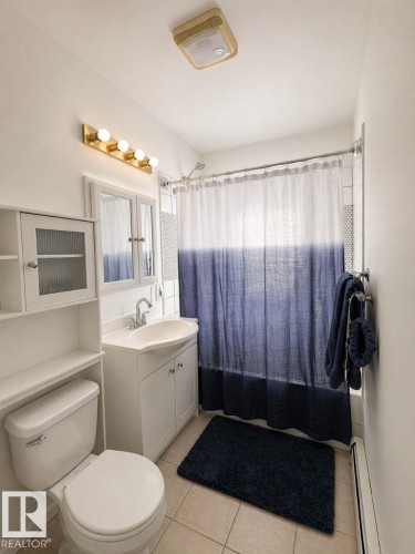 Compact bathroom featuring a white vanity with cabinet storage, a wall-mounted medicine cabinet, and a built-in shelving unit - 11242 56 Street, Edmonton, AB - Indoor Photo Showing Bathroom