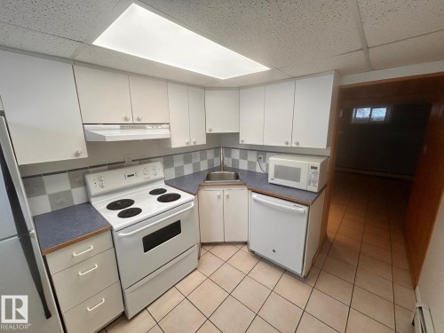 Kitchen featuring white cabinetry, checkered tile backsplash, a white electric range, a white dishwasher, and tile flooring - 11242 56 Street, Edmonton, AB - Indoor Photo Showing Kitchen