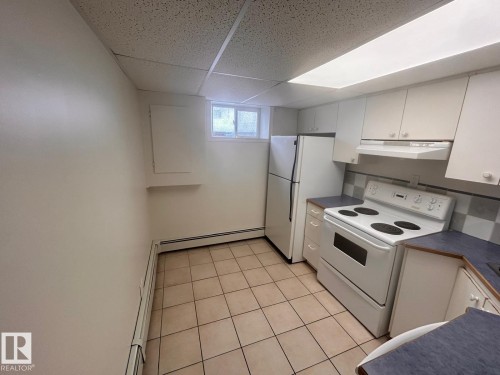 Kitchen featuring white cabinetry, a tile backsplash, white appliances, and a fluorescent ceiling light fixture - 11242 56 Street, Edmonton, AB - Indoor