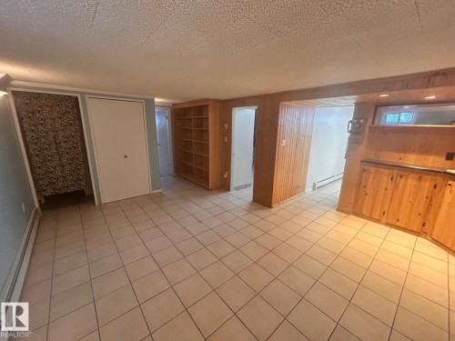 Spacious room featuring light-toned tile flooring, built-in wooden shelving, and warm wood paneling - 11242 56 Street, Edmonton, AB - Indoor
