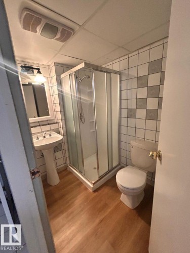 Bathroom featuring a corner shower enclosure with a clear glass door, a pedestal sink with dual-handle faucet, and wood-finish flooring - 11242 56 Street, Edmonton, AB - Indoor Photo Showing Bathroom