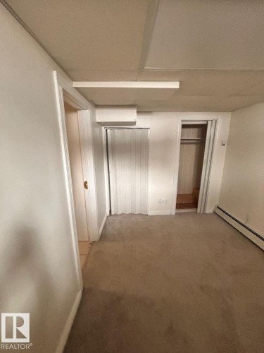 Carpeted room featuring a drop ceiling with integrated lighting, a built-in closet with bifold doors, a second closet with an open interior, and baseboard heating - 11242 56 Street, Edmonton, AB - Indoor Photo Showing Other Room