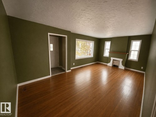 Spacious living area featuring wood-finish flooring, a decorative fireplace with a wood mantel, multiple windows, and a front entry door with a decorative glass insert - 11242 56 Street, Edmonton, AB - Indoor