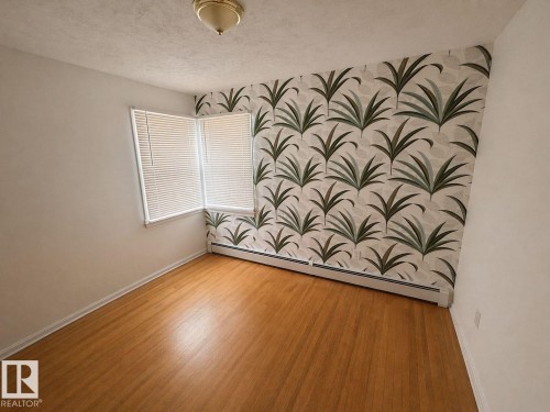 Room featuring wood-finish flooring, a corner window with horizontal blinds, and a decorative accent wall - 11242 56 Street, Edmonton, AB - Indoor Photo Showing Other Room
