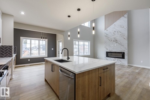 Kitchen island with light wood-finish cabinetry, white countertop, and integrated stainless steel dishwasher - 917 Elderberry Landing, Edmonton, AB - Indoor Photo Showing Kitchen With Fireplace With Upgraded Kitchen