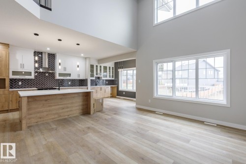 Expansive open-concept living area featuring a kitchen island with a light wood-finish base and light-toned countertop, contrasting dark herringbone backsplash, and pendant lighting - 917 Elderberry Landing, Edmonton, AB - Indoor