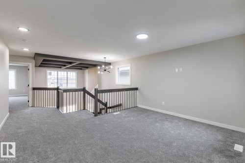 Spacious second-story landing featuring gray carpet, a dark wood-finish railing with vertical spindles, and a dark wood-finish coffered ceiling accent - 917 Elderberry Landing, Edmonton, AB - Indoor Photo Showing Other Room