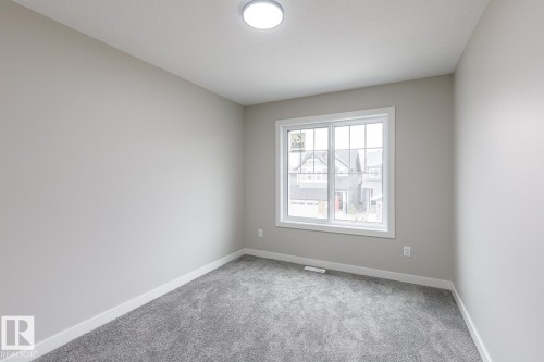 Neutral-toned room featuring a large window with white trim, gray plush carpeting, and a flush-mount ceiling light fixture - 917 Elderberry Landing, Edmonton, AB - Indoor Photo Showing Other Room