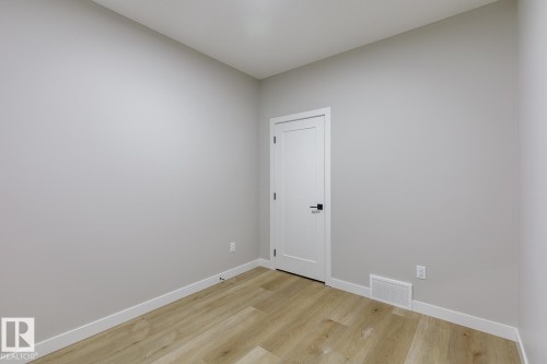 Neutral-toned room featuring light wood-finish flooring, white baseboards, and a contemporary white door with matte black hardware - 917 Elderberry Landing, Edmonton, AB - Indoor Photo Showing Other Room