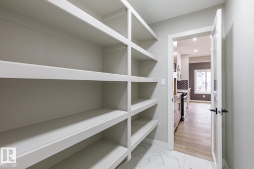 Walk-in pantry featuring extensive built-in shelving, white marble-look flooring, and a frosted glass panel door - 917 Elderberry Landing, Edmonton, AB - Indoor With Storage