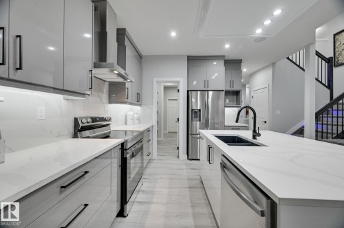 Modern kitchen featuring white countertops, light gray high-gloss cabinetry, stainless steel appliances, and wood-finish flooring - 1774 Crossbill Loop, Edmonton, AB - Indoor Photo Showing Kitchen With Double Sink With Upgraded Kitchen