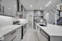 Modern kitchen featuring white countertops, light gray high-gloss cabinetry, stainless steel appliances, and wood-finish flooring - 