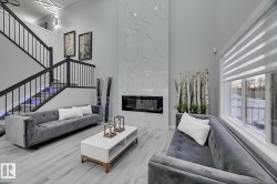 Two-story living room featuring a floor-to-ceiling fireplace with a sleek linear insert, light wood-finish flooring, a contemporary open-riser staircase with black metal balusters, large windows with horizontal blinds, and a modern ceiling light fixture - 