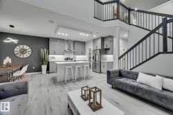 Open-concept living space featuring a modern kitchen with high-gloss cabinetry, a central island with a white countertop, and stainless steel appliances - 