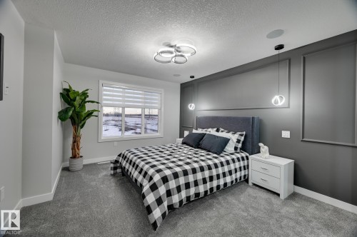 Accent wall featuring decorative molding, modern pendant lighting, and a fabric upholstered headboard - 1774 Crossbill Loop, Edmonton, AB - Indoor Photo Showing Bedroom