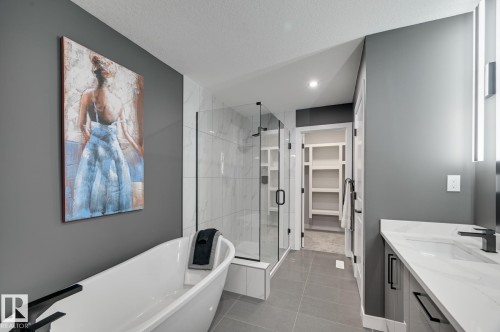 Bathroom featuring a freestanding tub, glass-enclosed shower with tile surround, single vanity with integrated sink, and dark tone flooring - 1774 Crossbill Loop, Edmonton, AB - Indoor Photo Showing Bathroom