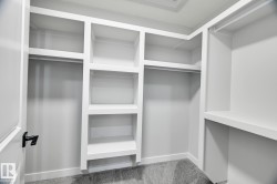 Walk-in closet featuring built-in shelving, multiple hanging rods, white-painted cabinetry, and gray carpet flooring - 