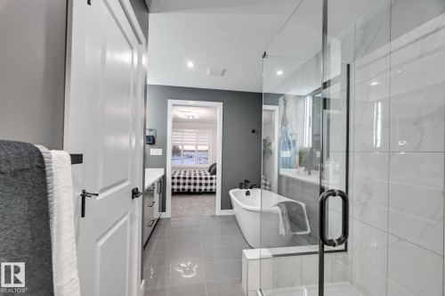 Bathroom featuring a freestanding soaking tub with matte black fixtures, a glass-enclosed shower with white tiled walls, and a long vanity with dual sinks and white countertops - 1774 Crossbill Loop, Edmonton, AB - Indoor Photo Showing Bathroom