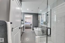 Bathroom featuring a freestanding soaking tub with matte black fixtures, a glass-enclosed shower with white tiled walls, and a long vanity with dual sinks and white countertops - 