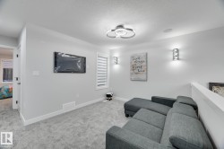 Carpeted room featuring a built-in wall-mounted television, modern ceiling light fixture, two decorative wall sconces, and a window with horizontal blinds - 