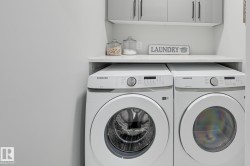 Dedicated laundry area featuring a white countertop, light gray upper cabinetry with black hardware, and bright white walls - 
