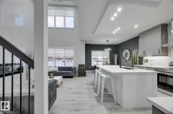 Open-concept living space featuring a gourmet kitchen with a large white island, integrated appliances, and light wood-finish flooring - 