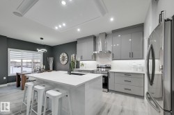 Open-concept kitchen featuring a large island with a white countertop, light gray wood-finish flooring, and white recessed lighting - 