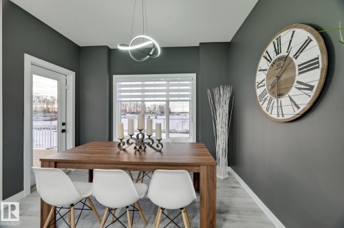 Dining area featuring a wood-finish table, light wood-finish flooring, a contemporary pendant light fixture, a window with horizontal blinds, and a glass-paneled exterior door - 1774 Crossbill Loop, Edmonton, AB - Indoor Photo Showing Dining Room