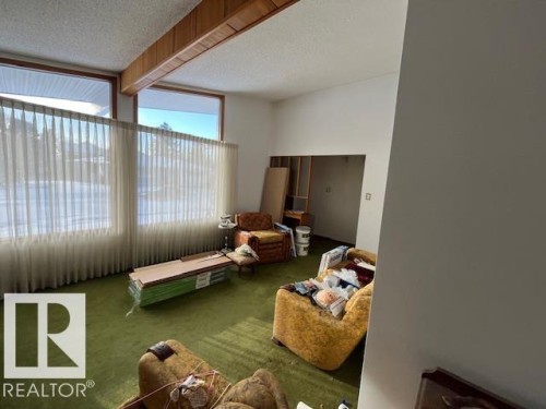 Spacious interior featuring a large window with vertical blinds, green carpeting, and a wooden ceiling beam - 11003 144 Street, Edmonton, AB - Indoor