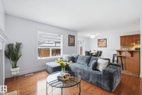 Open concept living area featuring wood-finish flooring, a white trim window, a chandelier in the dining space, a breakfast bar, and warm-toned kitchen cabinetry - 3016 24 Ave, Edmonton, AB - Indoor Photo Showing Living Room