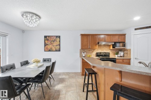 Open-concept kitchen featuring wood cabinetry, a tiled backsplash, and a breakfast bar with stone-finish countertops - 3016 24 Ave, Edmonton, AB - Indoor