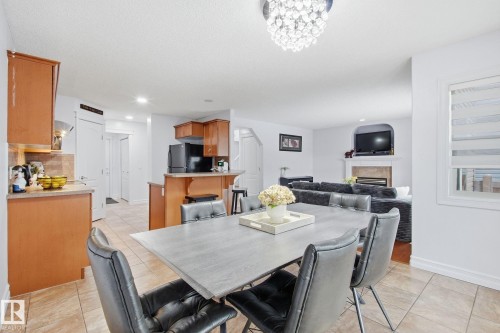 Open-concept living space featuring a dining area with a contemporary chandelier, a kitchen with wood cabinetry and a tile backsplash, and a living room with a fireplace and archway detail - 3016 24 Ave, Edmonton, AB - Indoor Photo Showing Dining Room