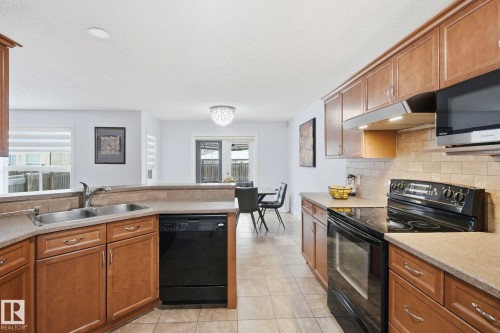 Kitchen featuring wood cabinetry, stone-finish countertops, and tile flooring - 3016 24 Ave, Edmonton, AB - Indoor Photo Showing Kitchen With Double Sink