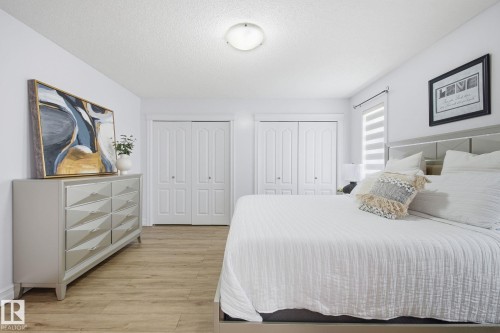 Brightly lit room featuring wood-finish flooring, two sets of bi-fold closet doors, and a ceiling-mounted light fixture - 3016 24 Ave, Edmonton, AB - Indoor Photo Showing Bedroom