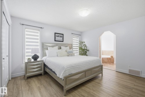 Bedroom featuring wood-finish flooring, two large windows with blinds, a double-door closet, an arched doorway, and a ceiling-mounted light fixture - 3016 24 Ave, Edmonton, AB - Indoor Photo Showing Bedroom
