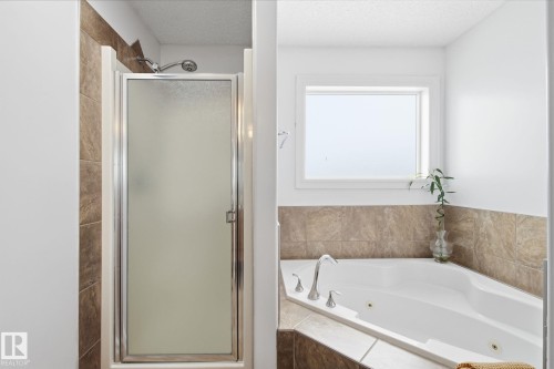 Tiled corner tub featuring chrome fixtures and an adjacent standing shower with a frosted glass door - 3016 24 Ave, Edmonton, AB - Indoor Photo Showing Bathroom