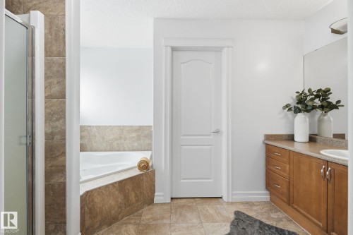 Bathroom featuring an integrated corner tub with tiled surround, a glass-enclosed shower, a wood-finish vanity with an integrated sink, and coordinated floor tiling - 3016 24 Ave, Edmonton, AB - Indoor Photo Showing Bathroom