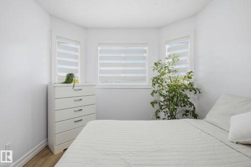 Bedroom featuring a bay window with contemporary privacy blinds, light wood-finish flooring, and crisp white wall paint - 3016 24 Ave, Edmonton, AB - Indoor Photo Showing Bedroom