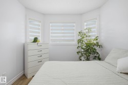 Bedroom featuring a bay window with contemporary privacy blinds, light wood-finish flooring, and crisp white wall paint - 