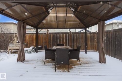 Expansive backyard deck featuring a brown gazebo with lighting, privacy curtains, and a high-quality wooden fence - 3016 24 Ave, Edmonton, AB - Outdoor With Exterior