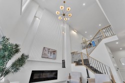 Two-story interior featuring a contemporary chandelier, a built-in electric fireplace, recessed lighting, a slatted accent wall, and a staircase with light wood handrails and black metal spindles - 