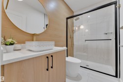 Modern bathroom featuring a wood-finish accent wall, gold-framed oval mirror, and a white vessel sink with a gold-tone faucet - 