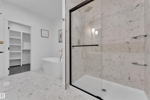 Spacious bathroom featuring a frameless glass shower enclosure with matte black hardware, large format speckled tile flooring, and a freestanding soaking tub - 247 Linden Loop, Leduc, AB - Indoor Photo Showing Bathroom