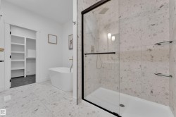 Spacious bathroom featuring a frameless glass shower enclosure with matte black hardware, large format speckled tile flooring, and a freestanding soaking tub - 