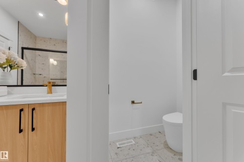 Bathroom featuring a light wood-finish vanity with white countertop, gold-finish faucet, and a large mirror with black framing - 247 Linden Loop, Leduc, AB - Indoor Photo Showing Other Room